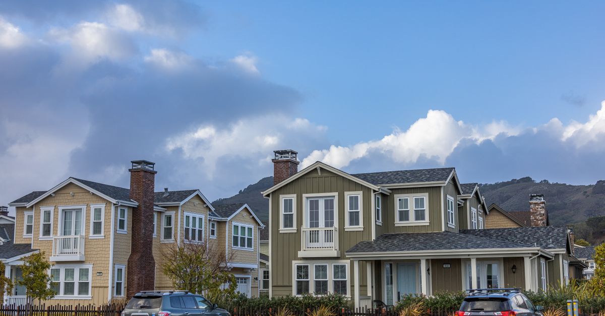 Picturesque suburban neighborhood with modern houses and parked cars under a partly cloudy sky.